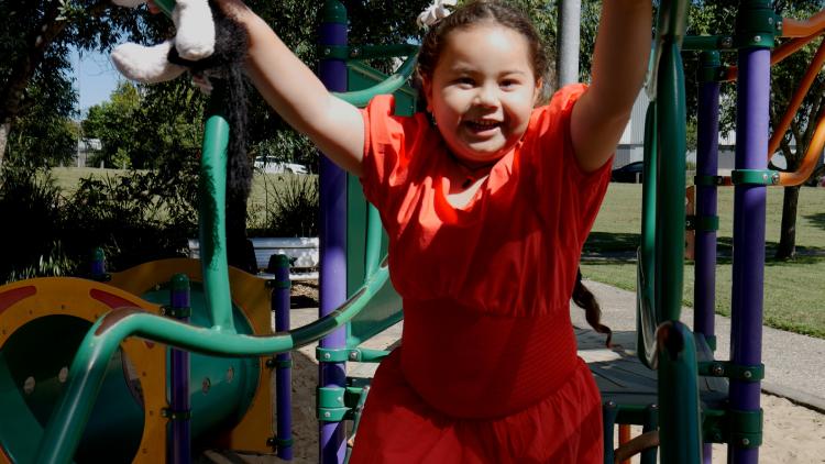 A young, happy girl in a red dress playing in a playground. 